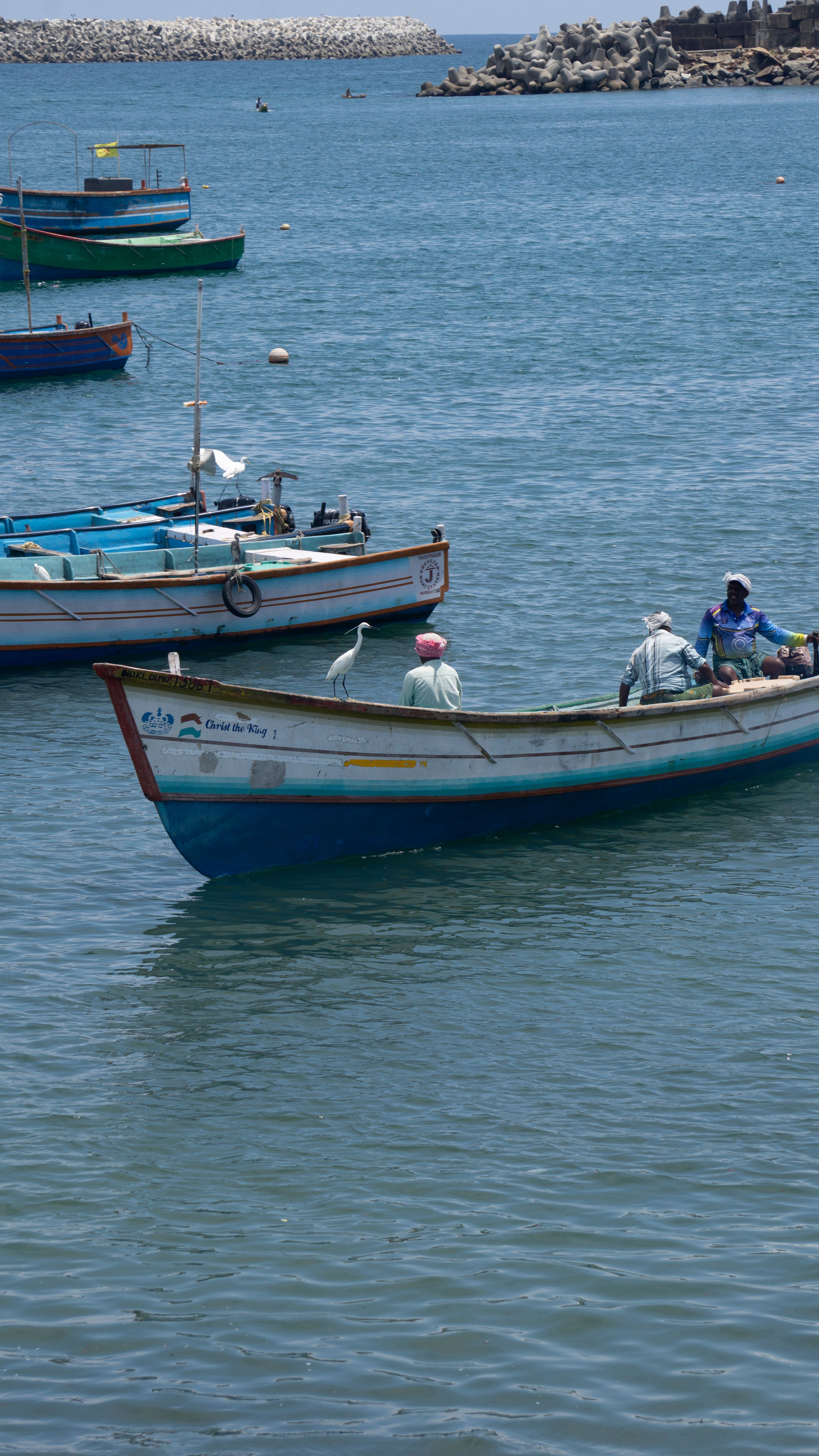 Fishermen in a traditional boat navigate calm sea waters on a clear, sunny day.