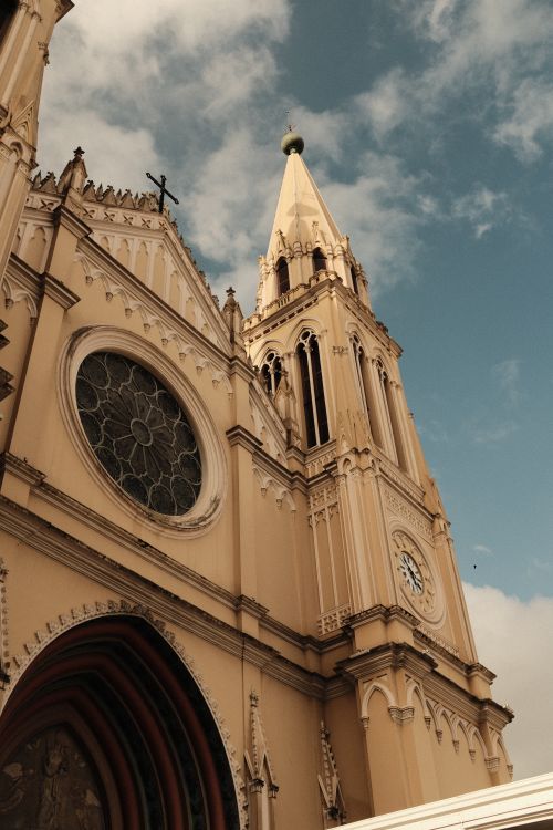 Free Detailed view of a gothic church facade with clock tower under a bright sky. Stock Photo