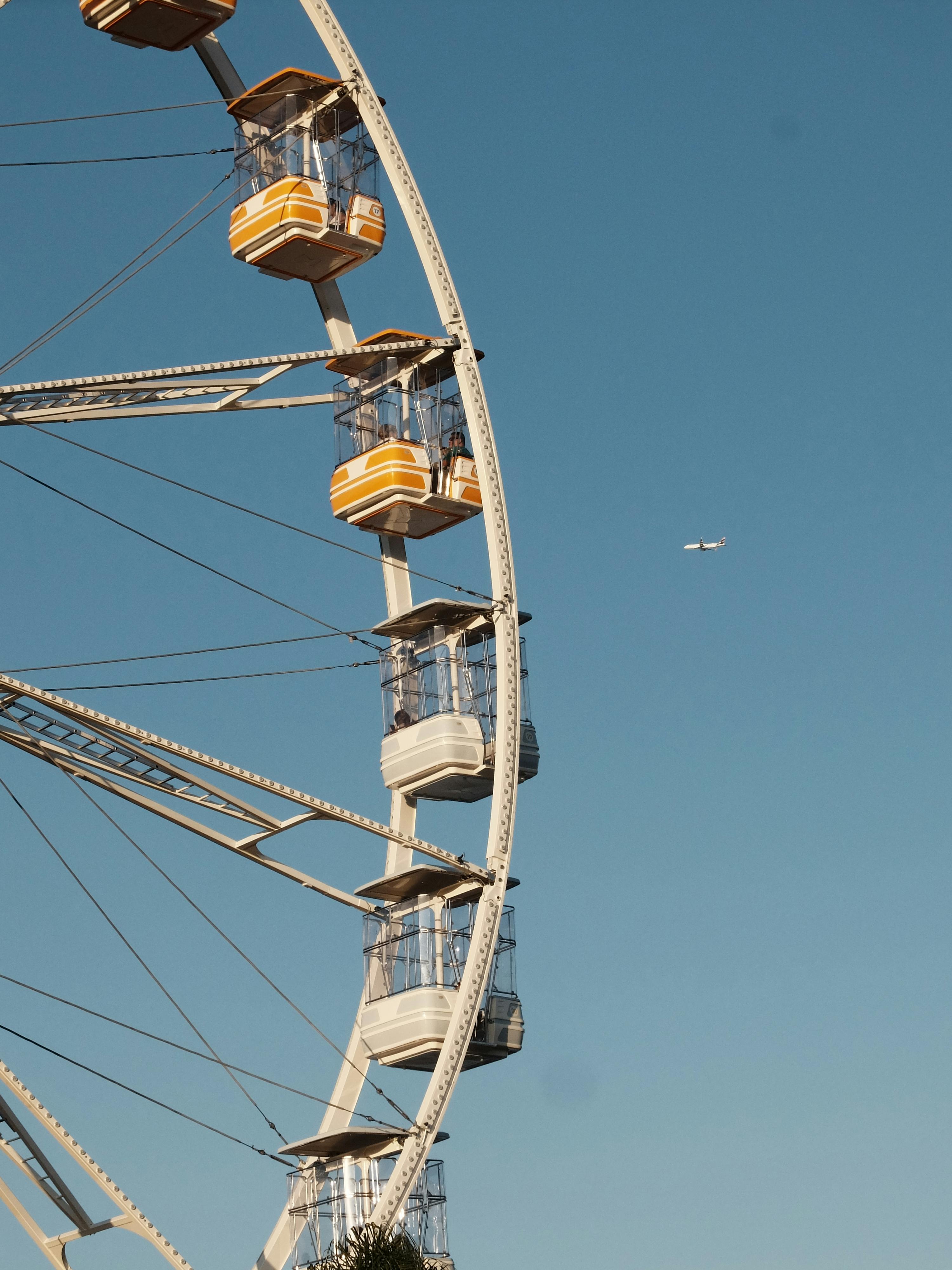 Ferris wheel with yellow cabins against a clear blue sky, hint of aerial travel.