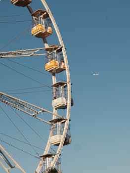 Ferris wheel with yellow cabins against a clear blue sky, hint of aerial travel.