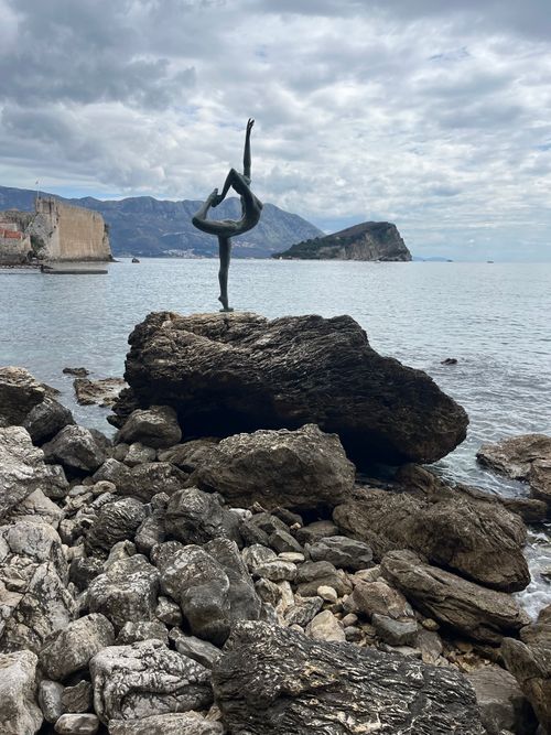 Free Elegant ballet statue on rocky shore in Budva, Montenegro, with mountain backdrop. Stock Photo