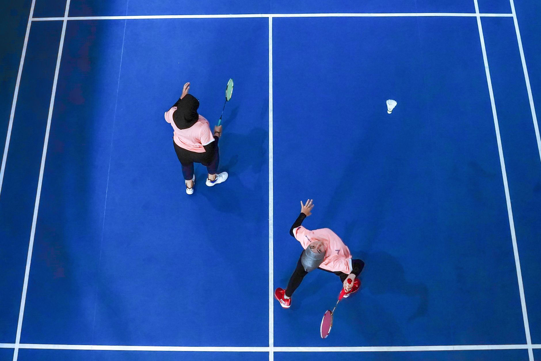 Top view of two women playing badminton on a blue court in Jakarta, Indonesia.