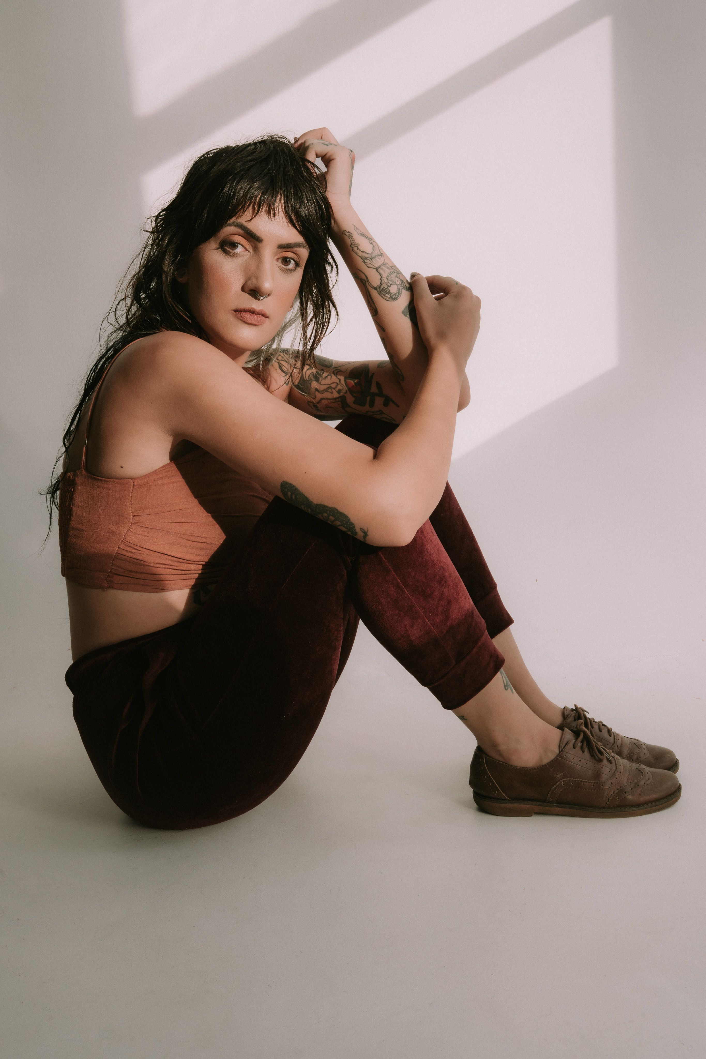 Artistic portrait of a woman in a studio, featuring natural light and a relaxed pose.