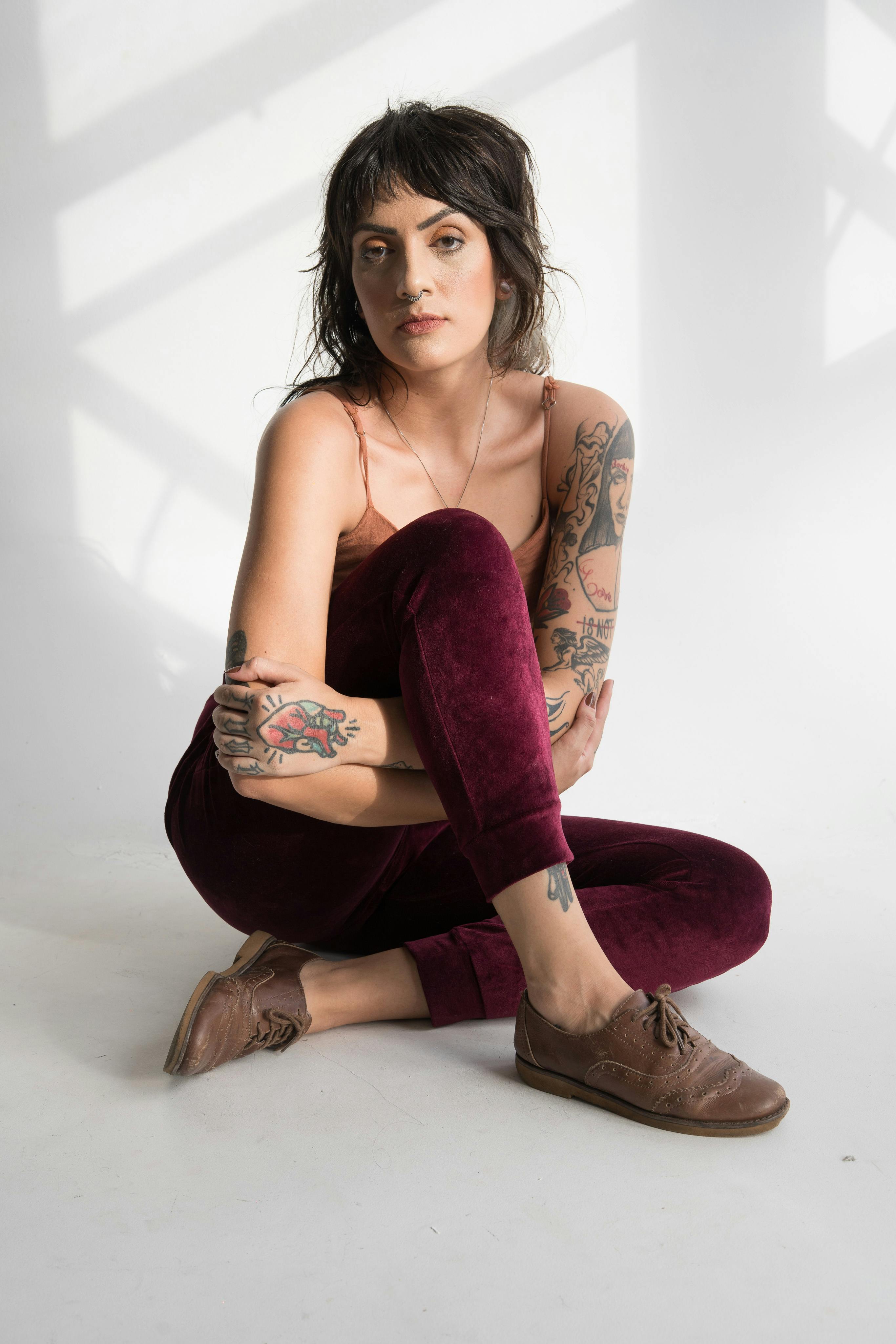 Portrait of a tattooed woman sitting gracefully in a studio, showcasing unique style and pose.