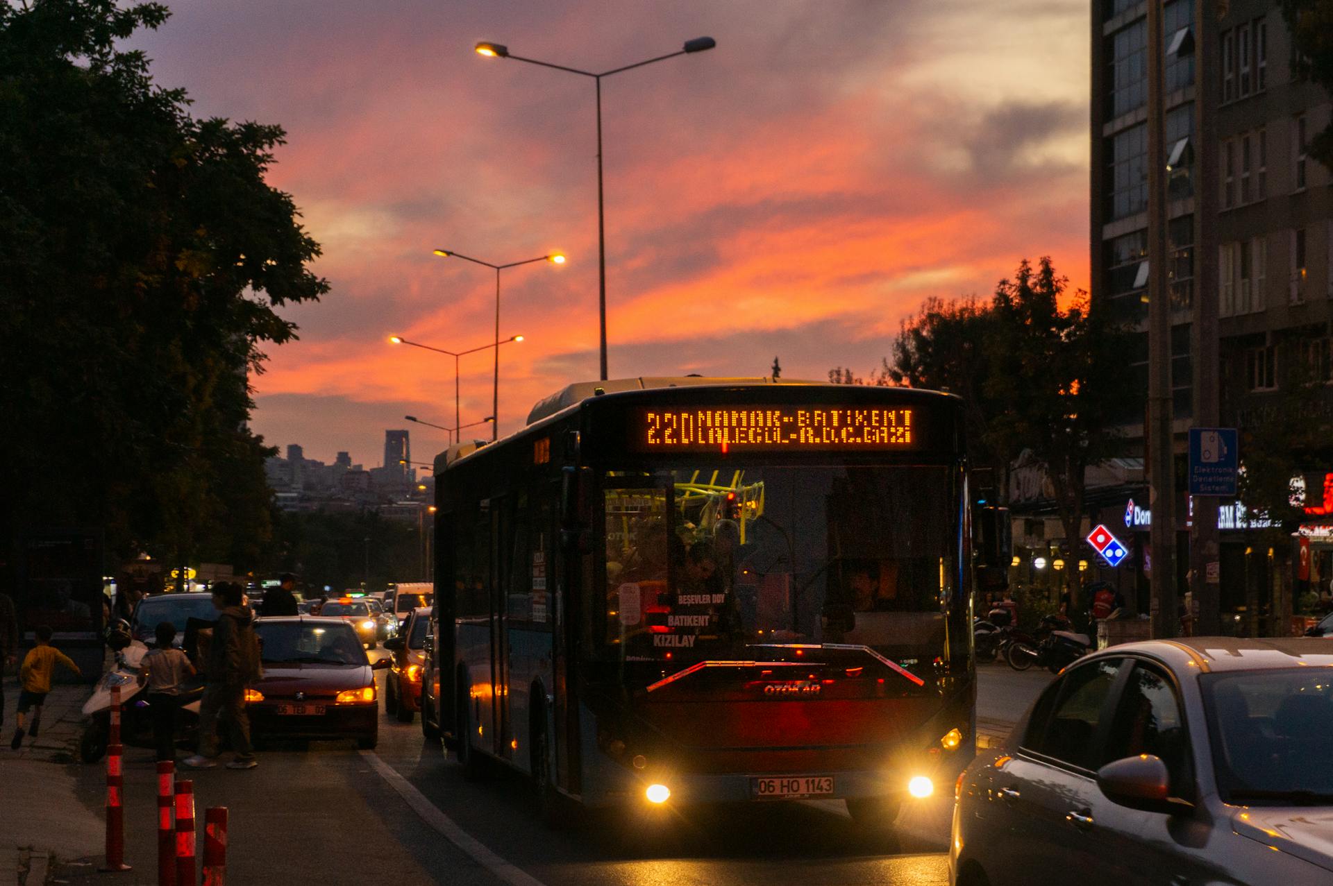 Urban street scene with a city bus and traffic at dusk, featuring a vibrant sunset.
