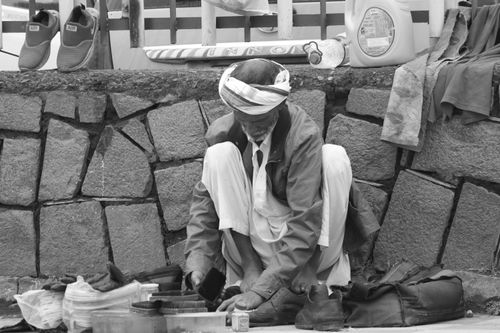 Free Black and white image of a street shoemaker polishing shoes outdoors. Stock Photo