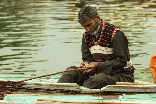 Free An elderly man fishing alone in a wooden boat on serene waters, captured during the day. Stock Photo