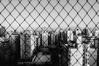 透过铁丝网栅栏，拍摄城市摩天大楼的单色视图，以突出城市建筑