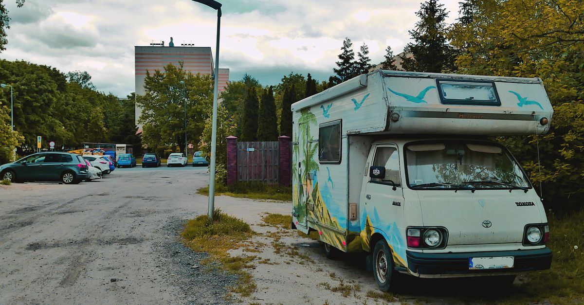 A colorful vintage camper van parked on a city street with trees and buildings in the background.