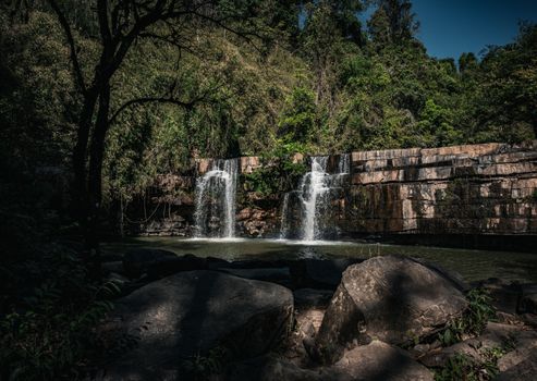Tranquil twin waterfalls cascade into a lush Thai forest, offering a nature escape.