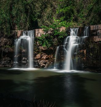 Breathtaking view of twin cascading waterfalls in a verdant Thai forest setting.