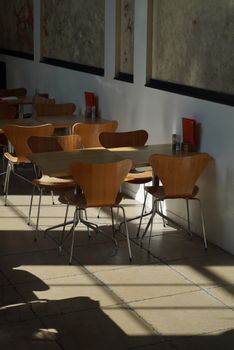 Sunlit cafe interior featuring empty wooden chairs and tables.