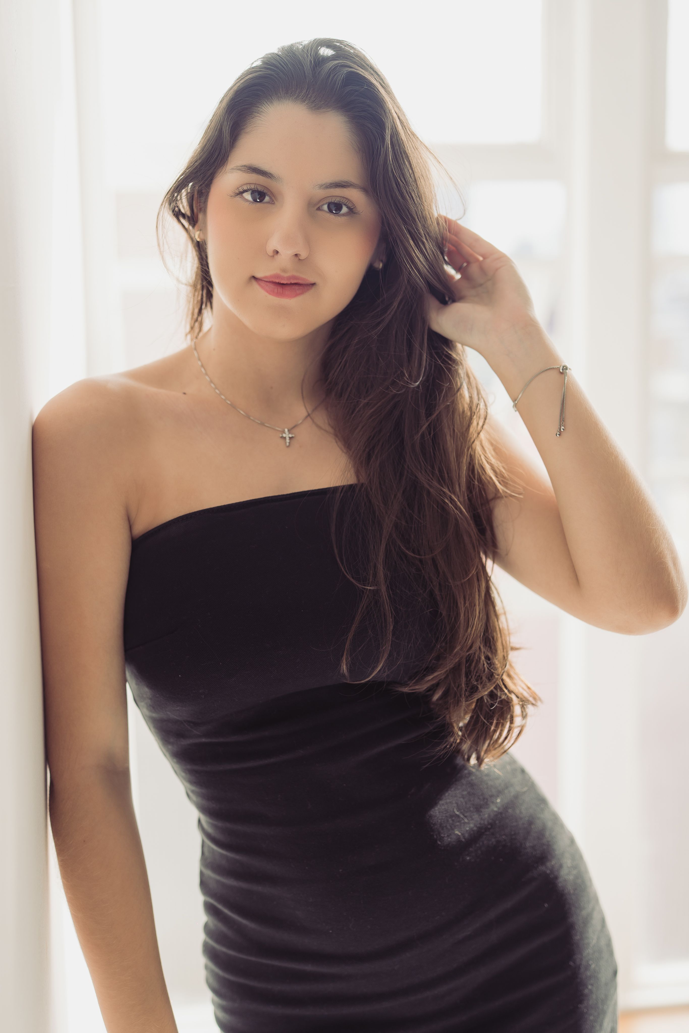 Portrait of a woman in a black dress by a window in Curitiba, Brazil.