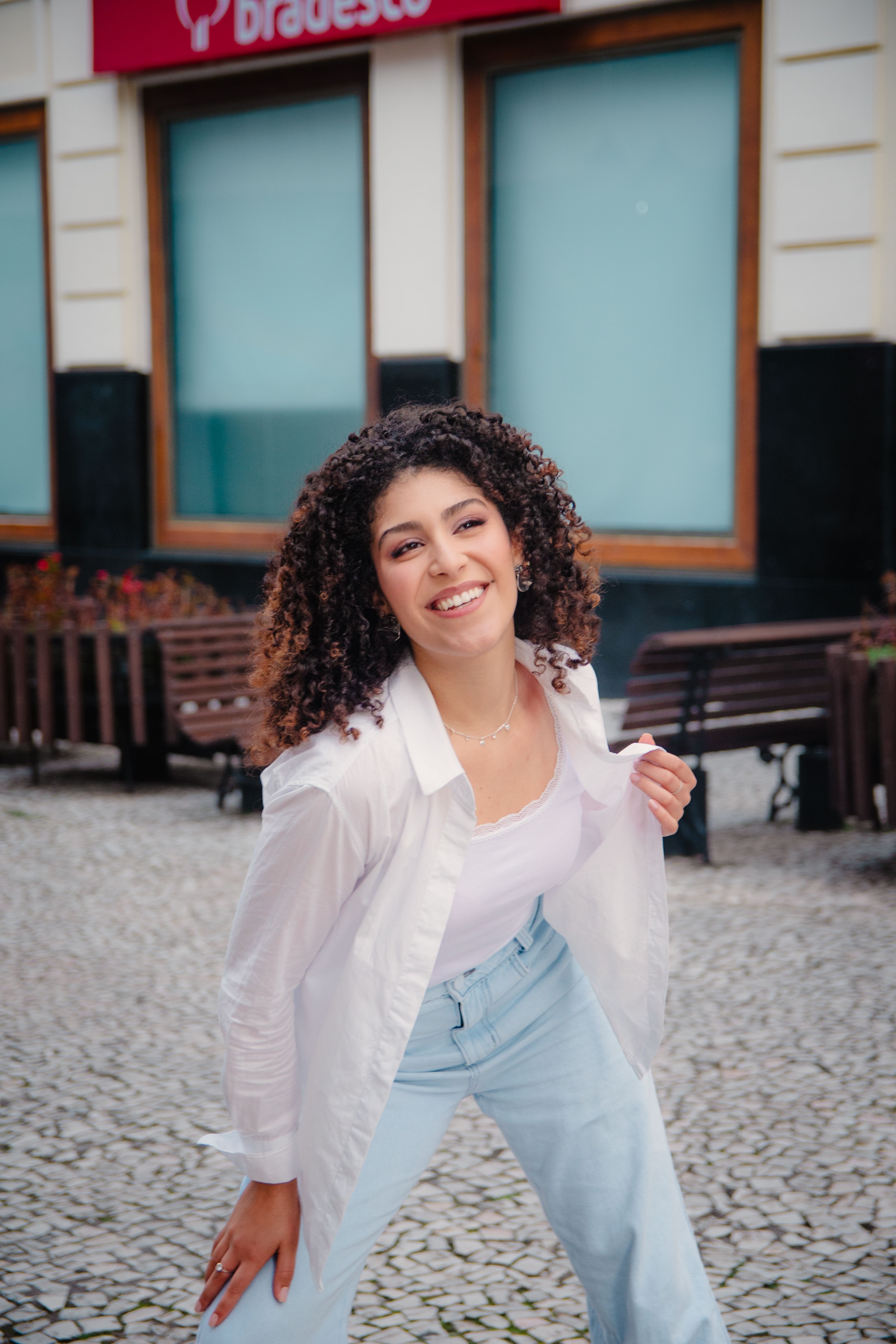 Joyful woman in casual attire posing outside on a cobblestone street.