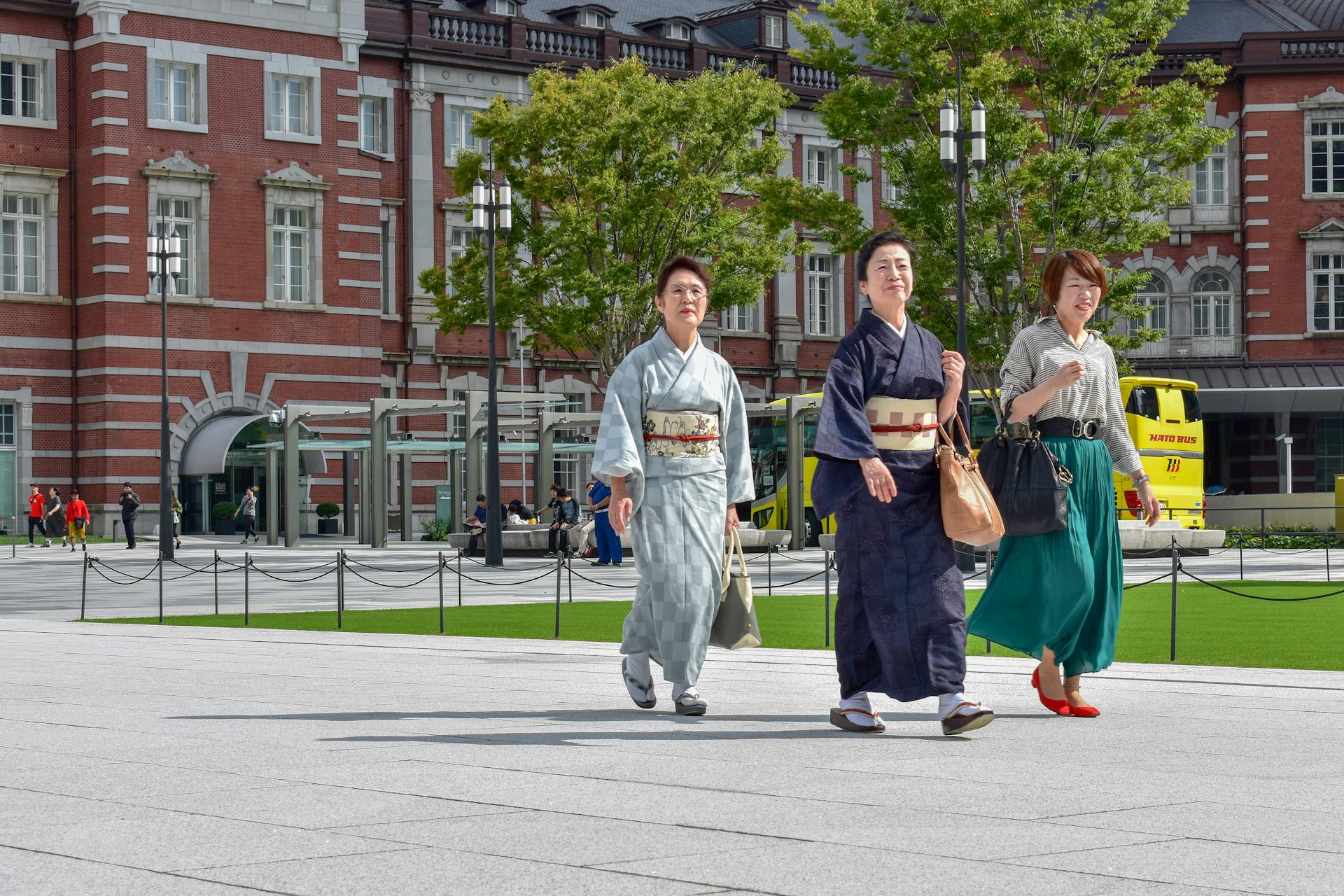 Three people in traditional attire walk outside Tokyo Station, Japan on a sunny day.