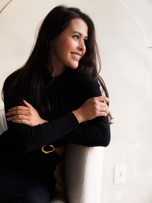 Free Portrait of a smiling woman in a black dress, seated indoors, with natural light and a modern background. Stock Photo