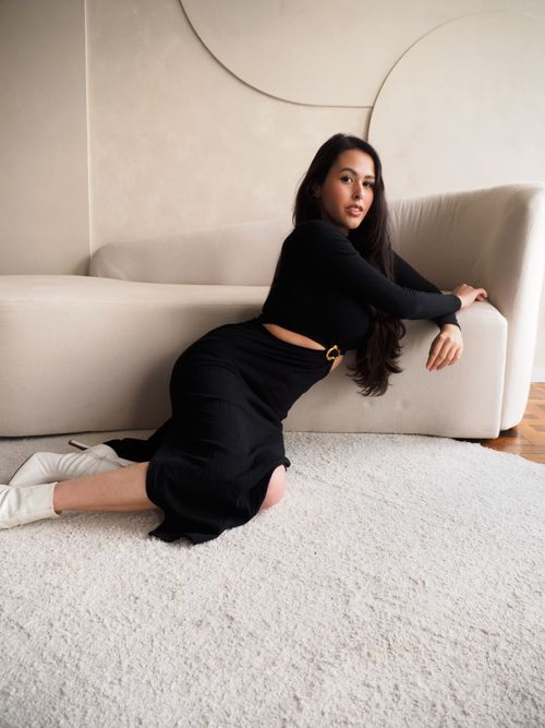Free Stylish woman in black dress posing indoors on a modern sofa, exuding elegance and confidence. Stock Photo