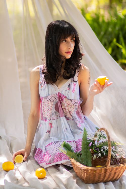 Free A young woman in a breezy dress enjoying a sunny day outdoors with lemons and a picnic basket. Stock Photo