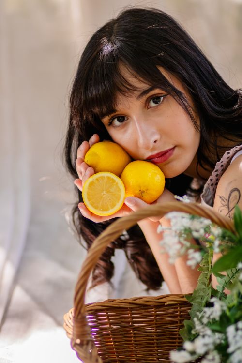 Free Portrait of a young woman holding fresh lemons in a wicker basket, set against a natural backdrop. Stock Photo