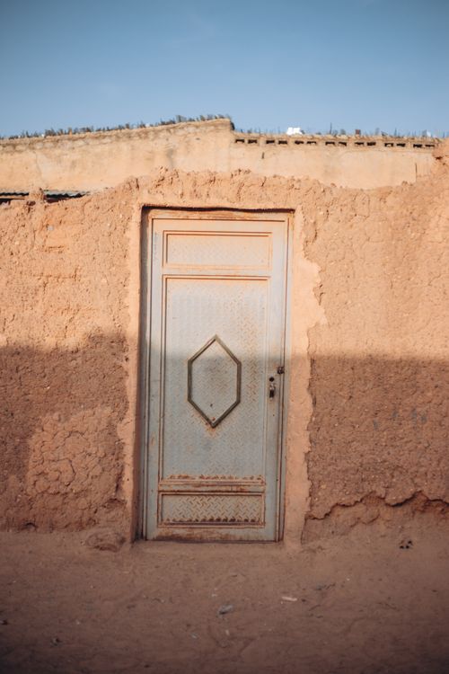 Free A vintage metal door embedded in a rustic mud wall under clear blue sky. Stock Photo