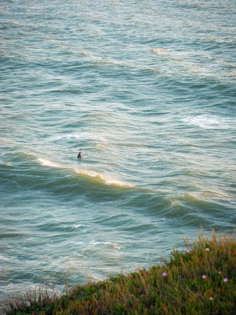 A lone surfer rides waves off the scenic California coastline during a stunning sunset.