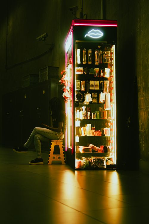 Free A person sitting beside a neon-lit vending machine in a dark, moody urban environment. Stock Photo