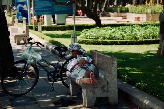 Man takes a nap on a park bench with a bicycle, enjoying a sunny day outdoors.