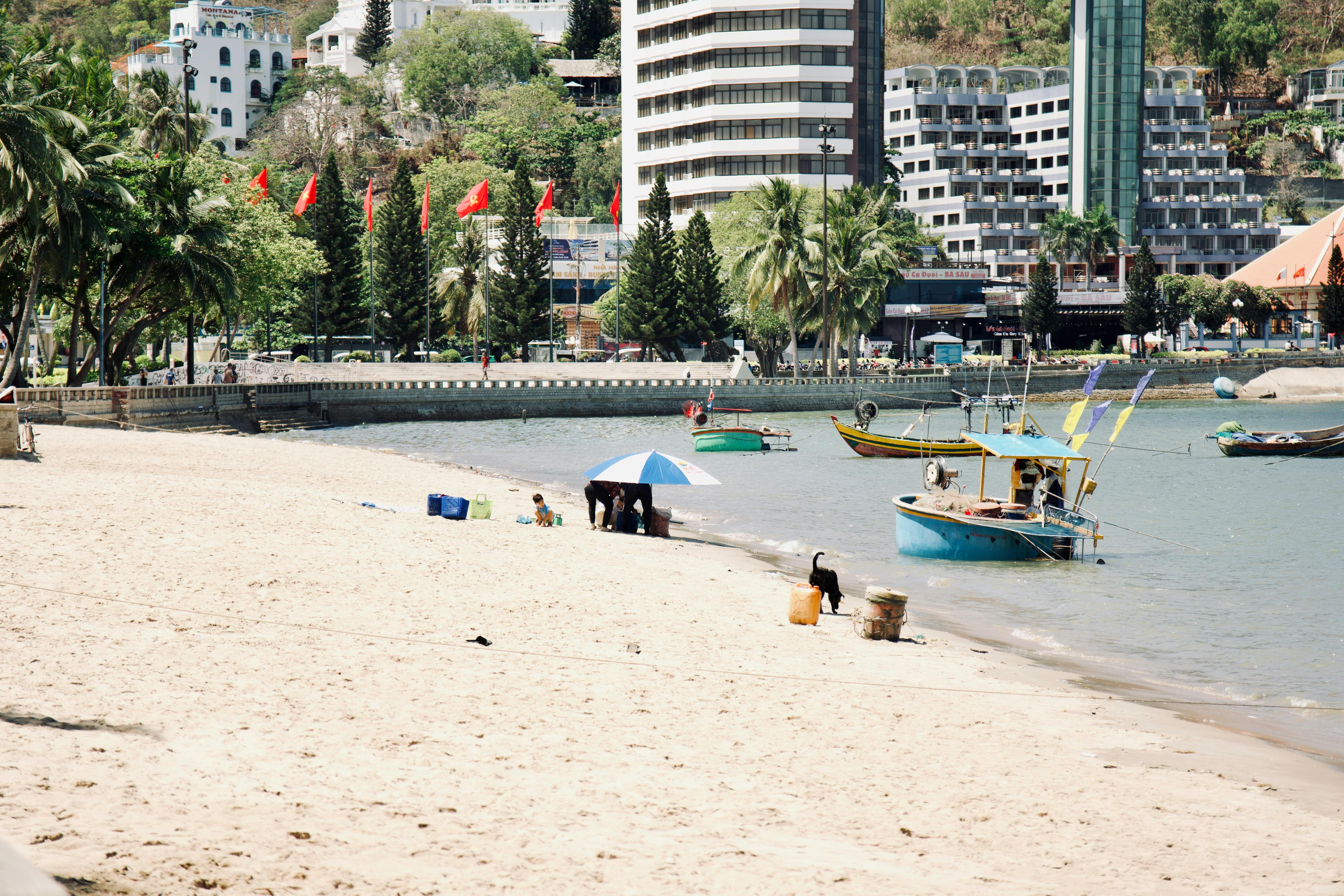 A vibrant beach scene with people enjoying the sand, boats docked, and a city skyline in the background.