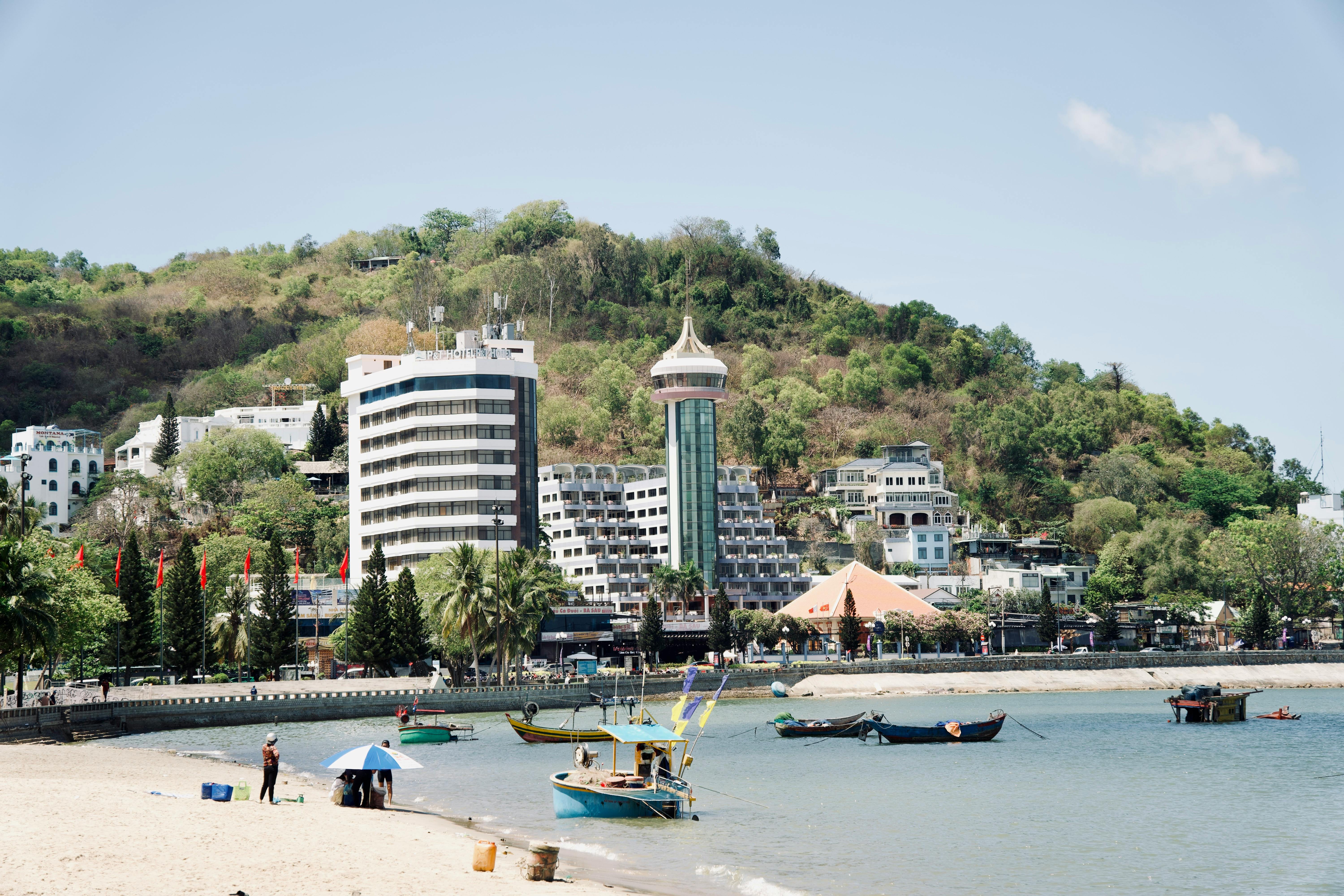 Tranquil beach in front of vibrant cityscape with lush hills and unique architecture.