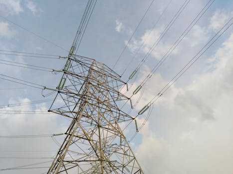 A close-up view of a high voltage transmission tower and lines against a cloudy sky.