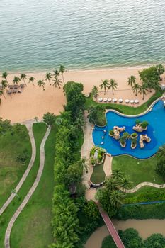 Aerial shot of a resort with pool, palm trees, and sandy beach in Chon Buri, Thailand.