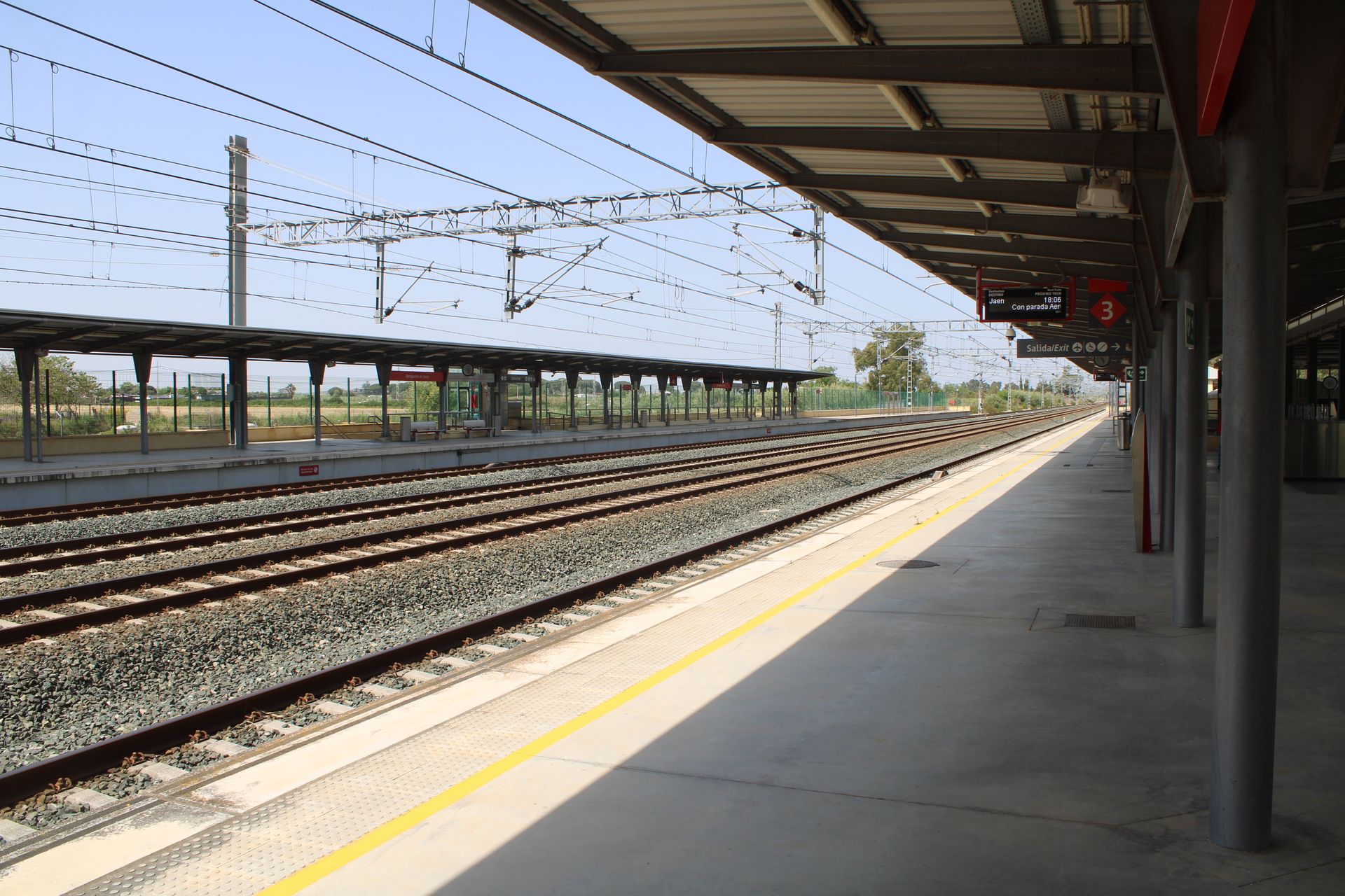 A quiet, sunlit railway station in Jerez de la Frontera, Spain, with expansive train tracks.