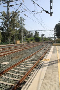 Explore the intricate railway tracks at a station in Jerez, framed by lush greenery under a bright sky.