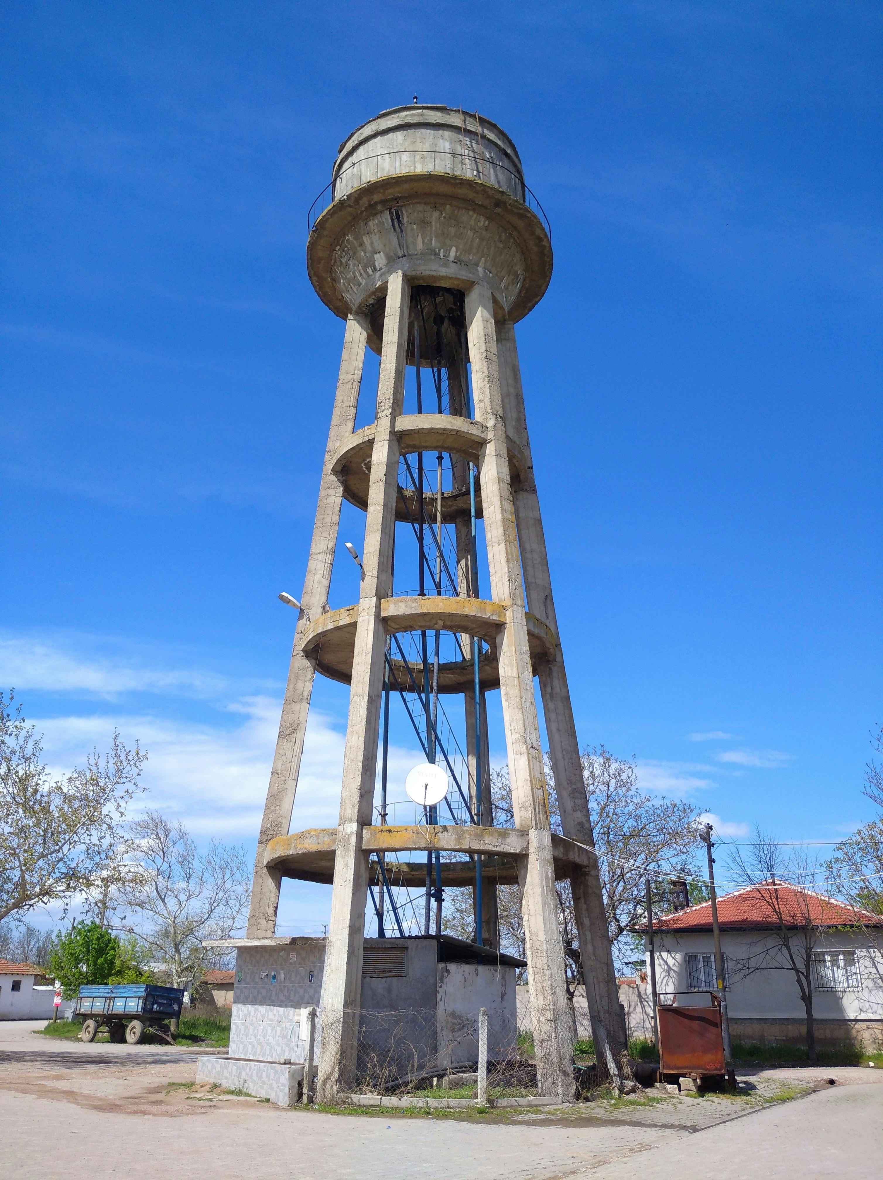 A tall concrete water tower stands prominently against a clear blue sky in Türkiye. | Indian Village Development