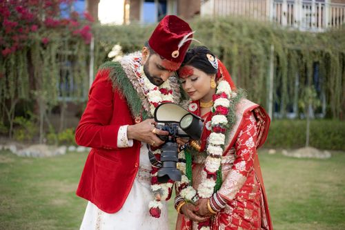 Free Indian bride and groom in traditional attire reviewing their wedding photos outdoors. Stock Photo