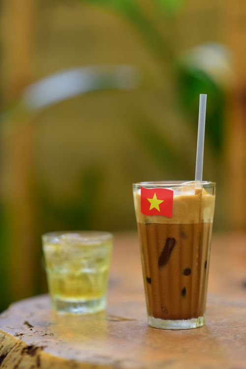 Free Refreshing glass of traditional Vietnamese iced coffee with a straw and a mini Vietnamese flag on a wooden table. Stock Photo