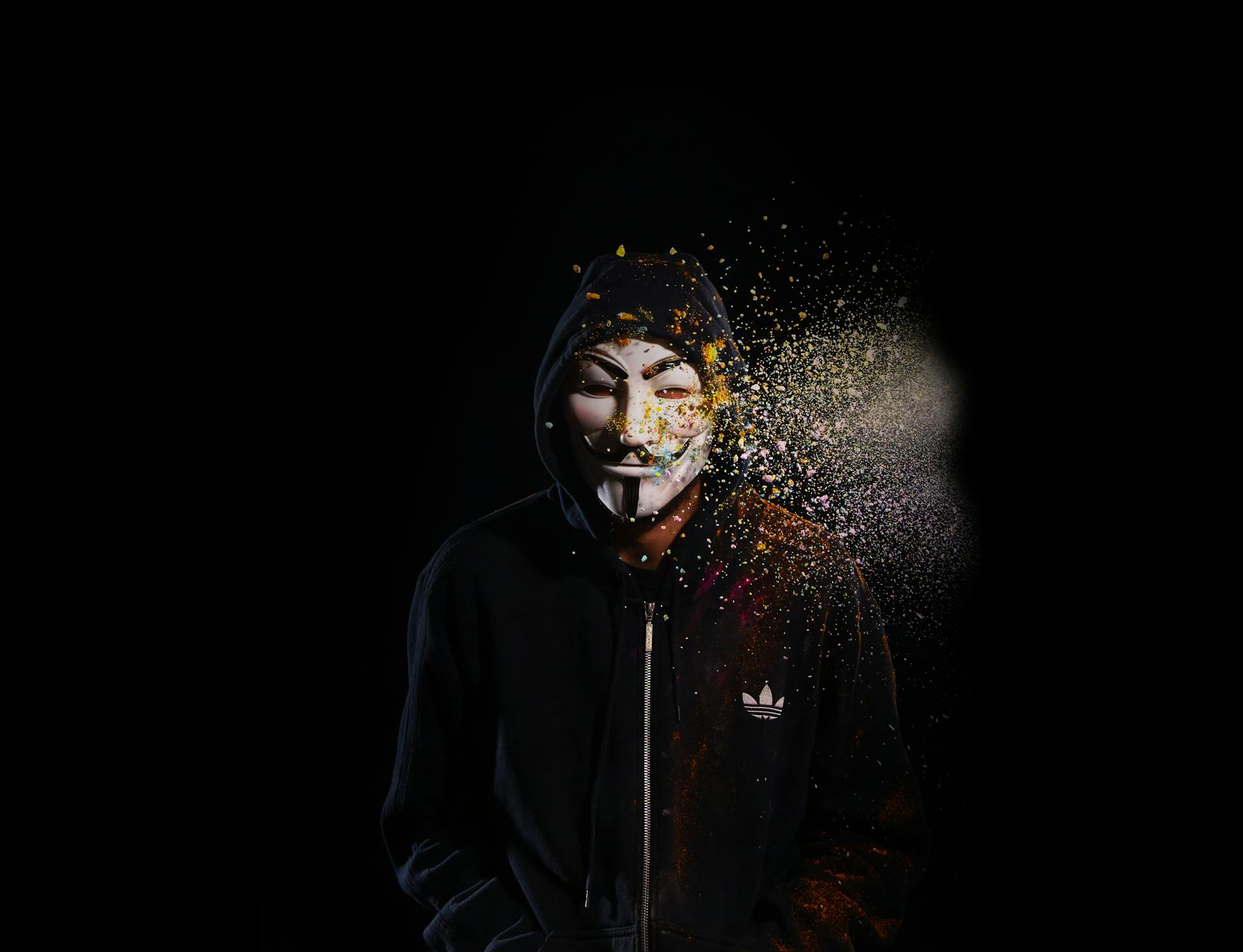 Mysterious figure in a hoodie with a striking Guy Fawkes mask against a dark background.