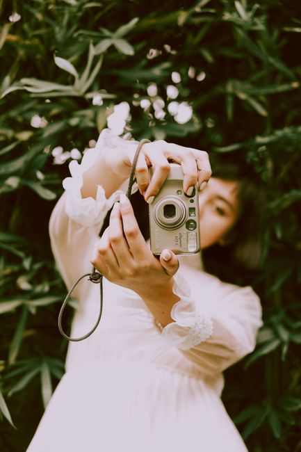 A woman poses with a camera amidst lush greenery, capturing the perfect outdoor moment.