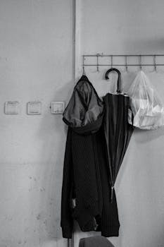 Monochrome scene of a coat, umbrella, and plastic bag hanging on a wall hook.