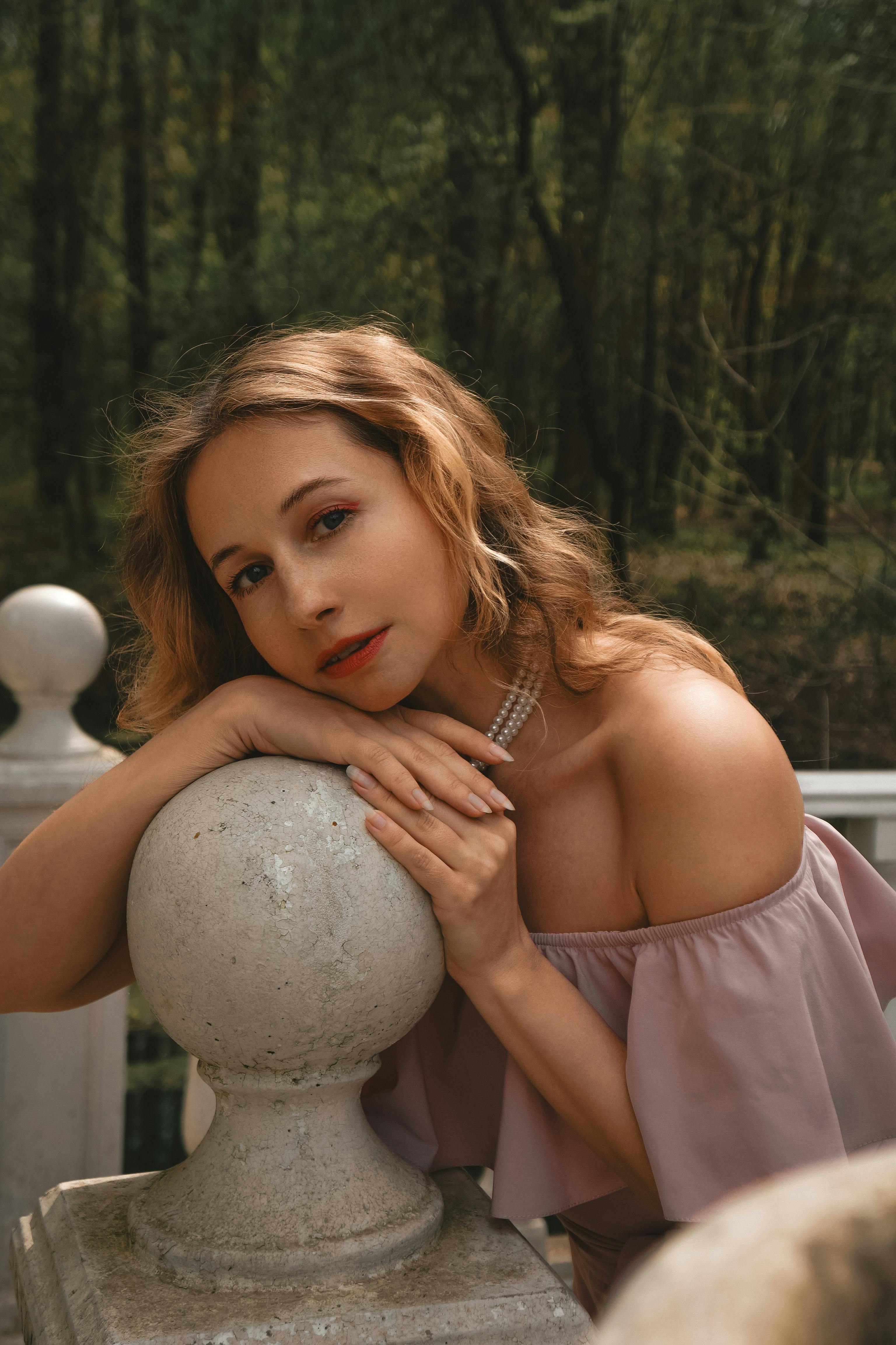 A serene portrait of an elegant woman leaning on a stone railing amidst a lush forest backdrop.