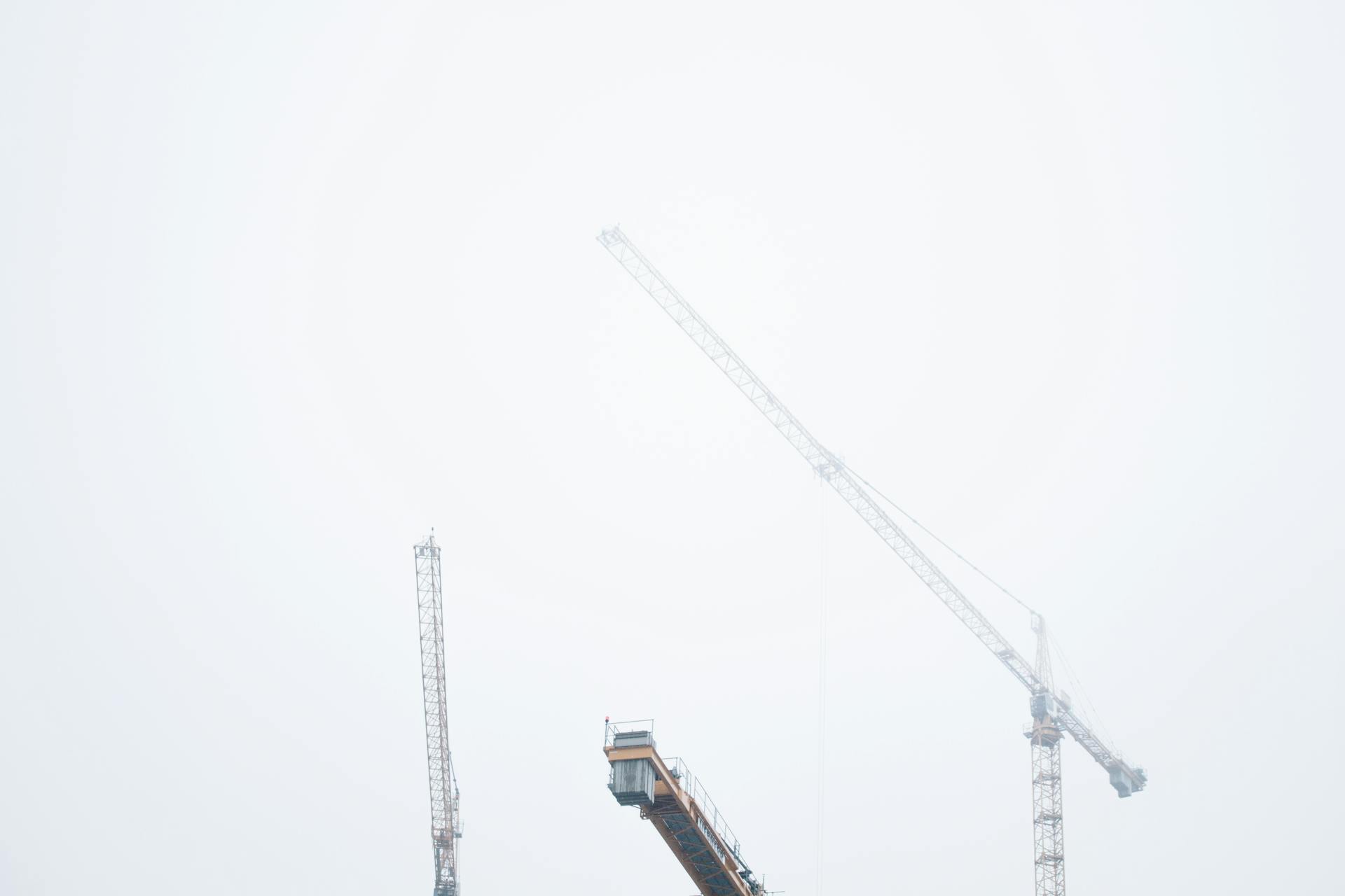 A foggy morning view of tower cranes at a construction site, creating an impressive industrial skyline.