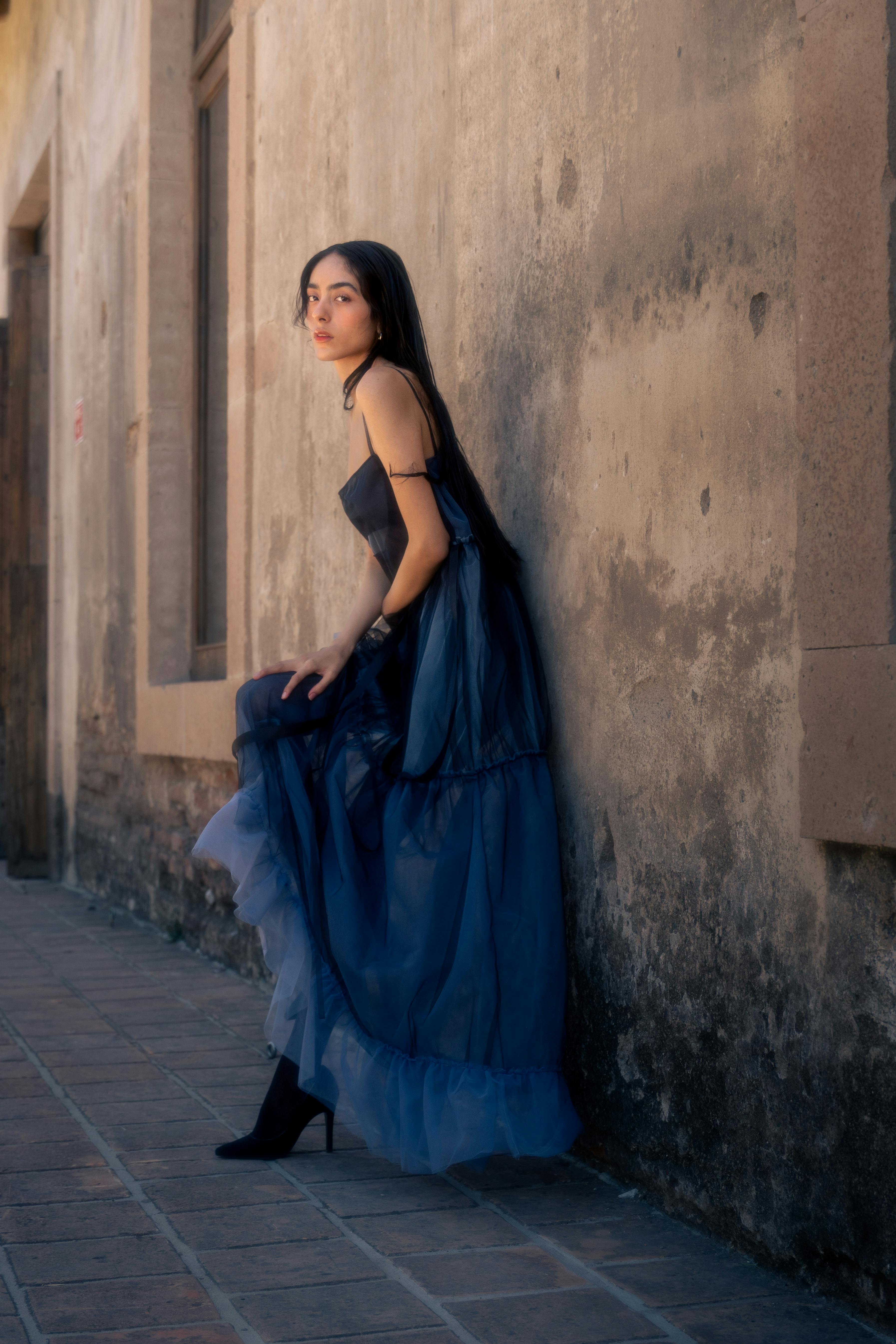 Free Stylish woman in a blue dress poses gracefully against a rustic wall, showcasing elegance and fashion. Stock Photo