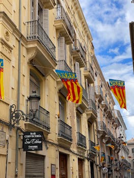 Charming facade in Valencia adorned with regional flags under a blue sky.