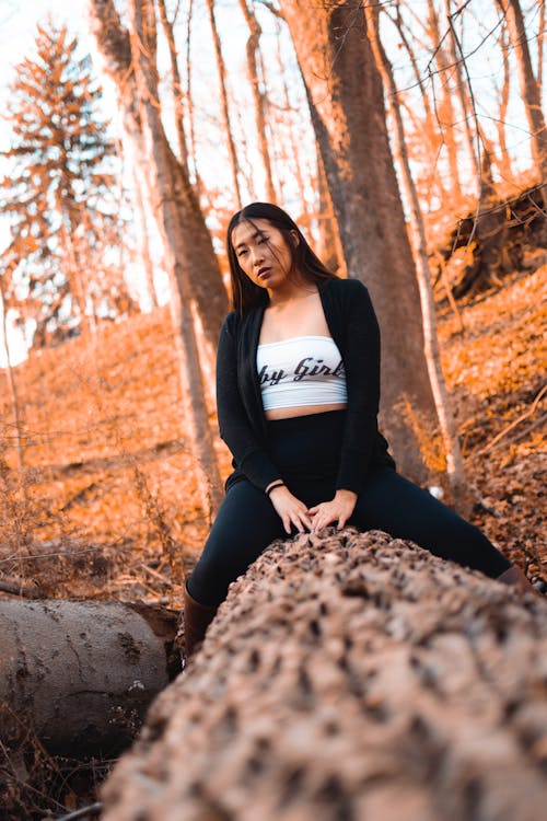 Selective Focus Photography of Woman in Black Cardigan Sitting on Fallen Tree Trunk