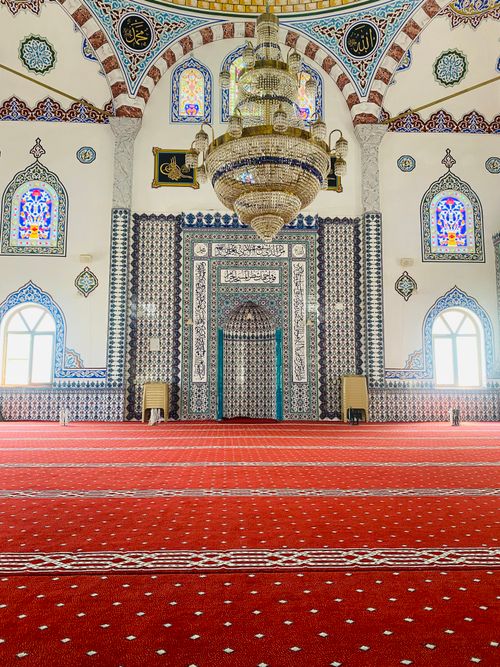 Free Intricate mosque interior featuring a grand chandelier and vibrant tilework with red carpet. Stock Photo