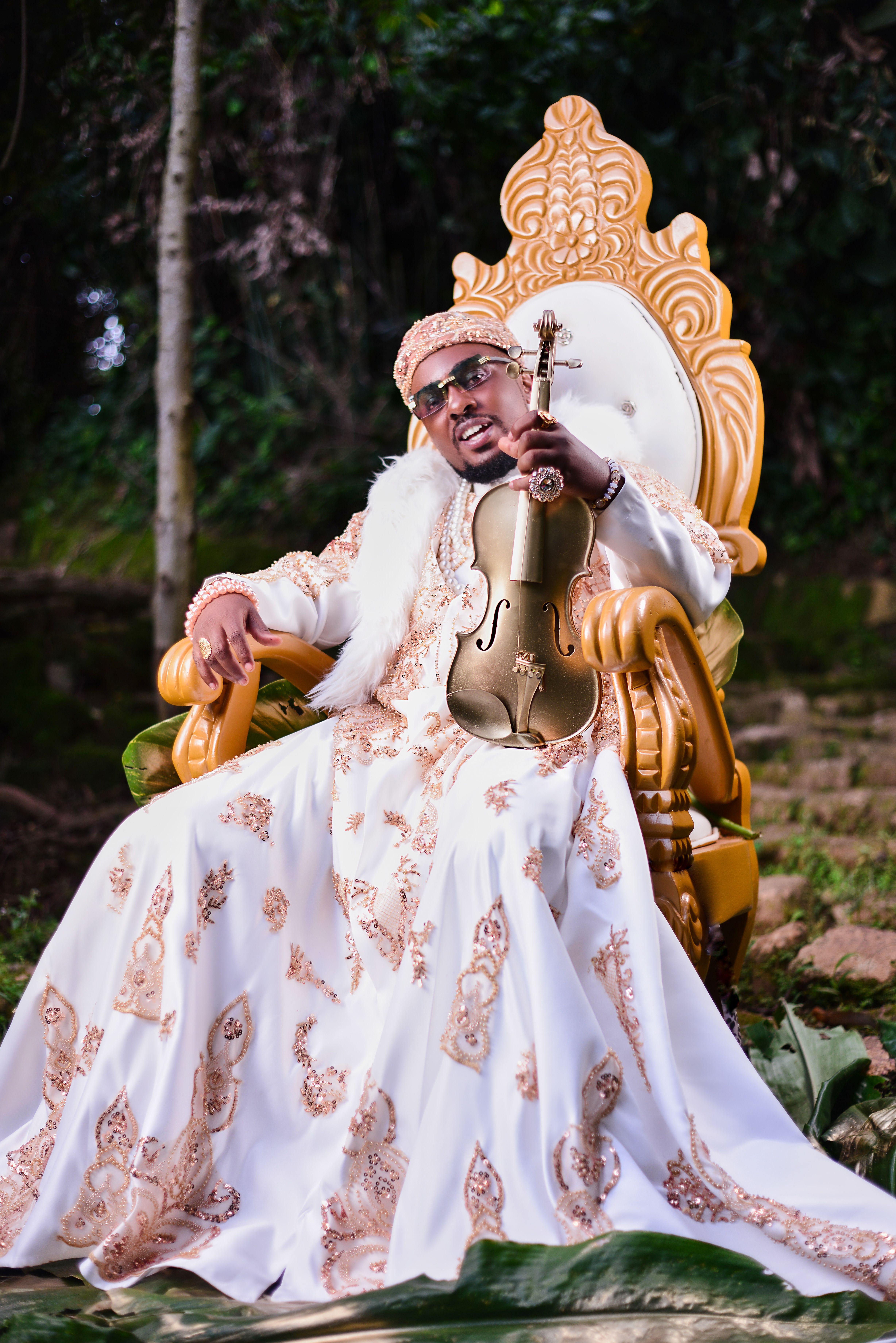 Musician in luxurious attire seated outdoors with a violin, exuding elegance and style.