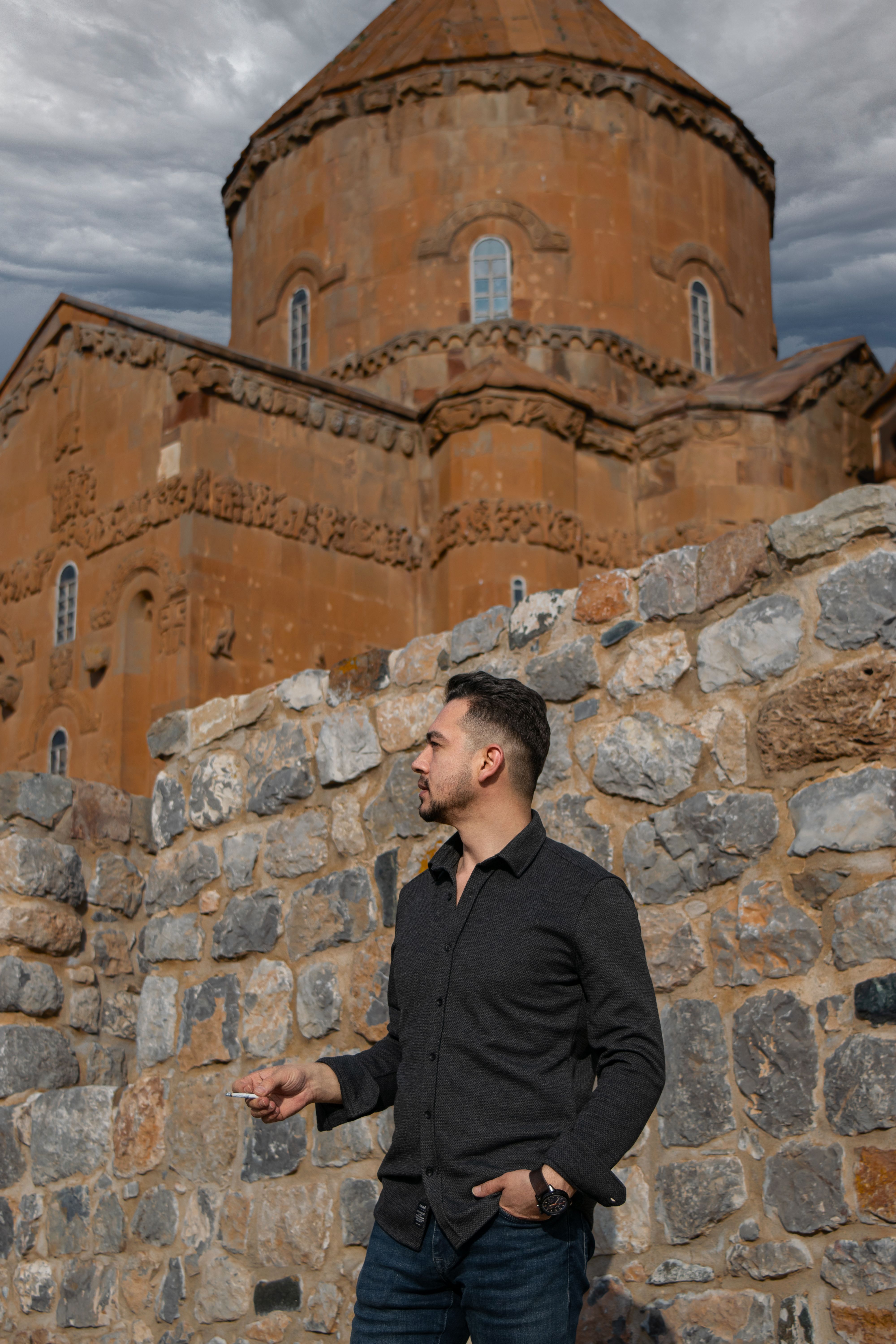 A man standing beside the ancient Akdamar Church in Van, Türkiye, showcasing its historical architecture.