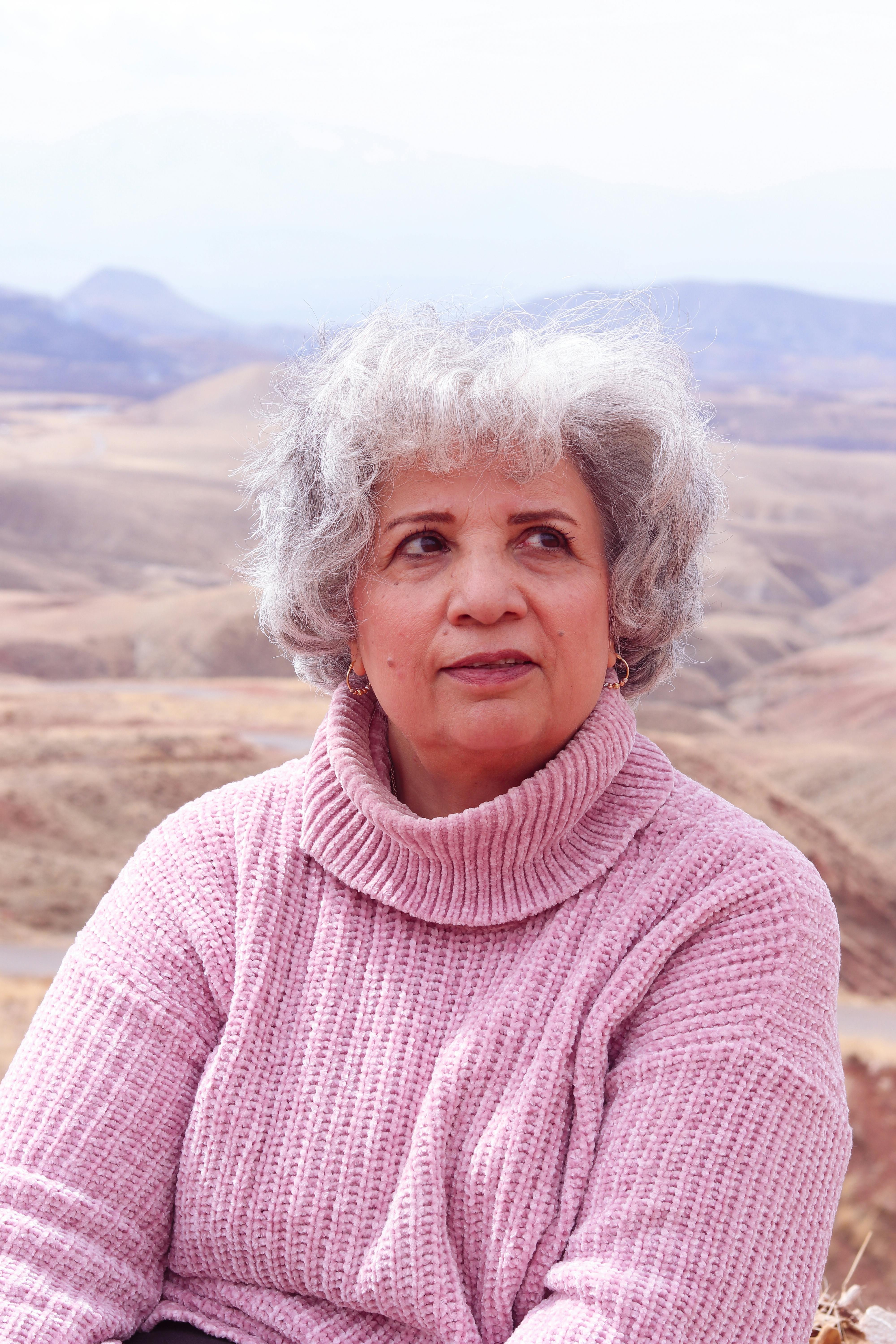 Senior woman in pink sweater enjoying a peaceful moment in the mountains.