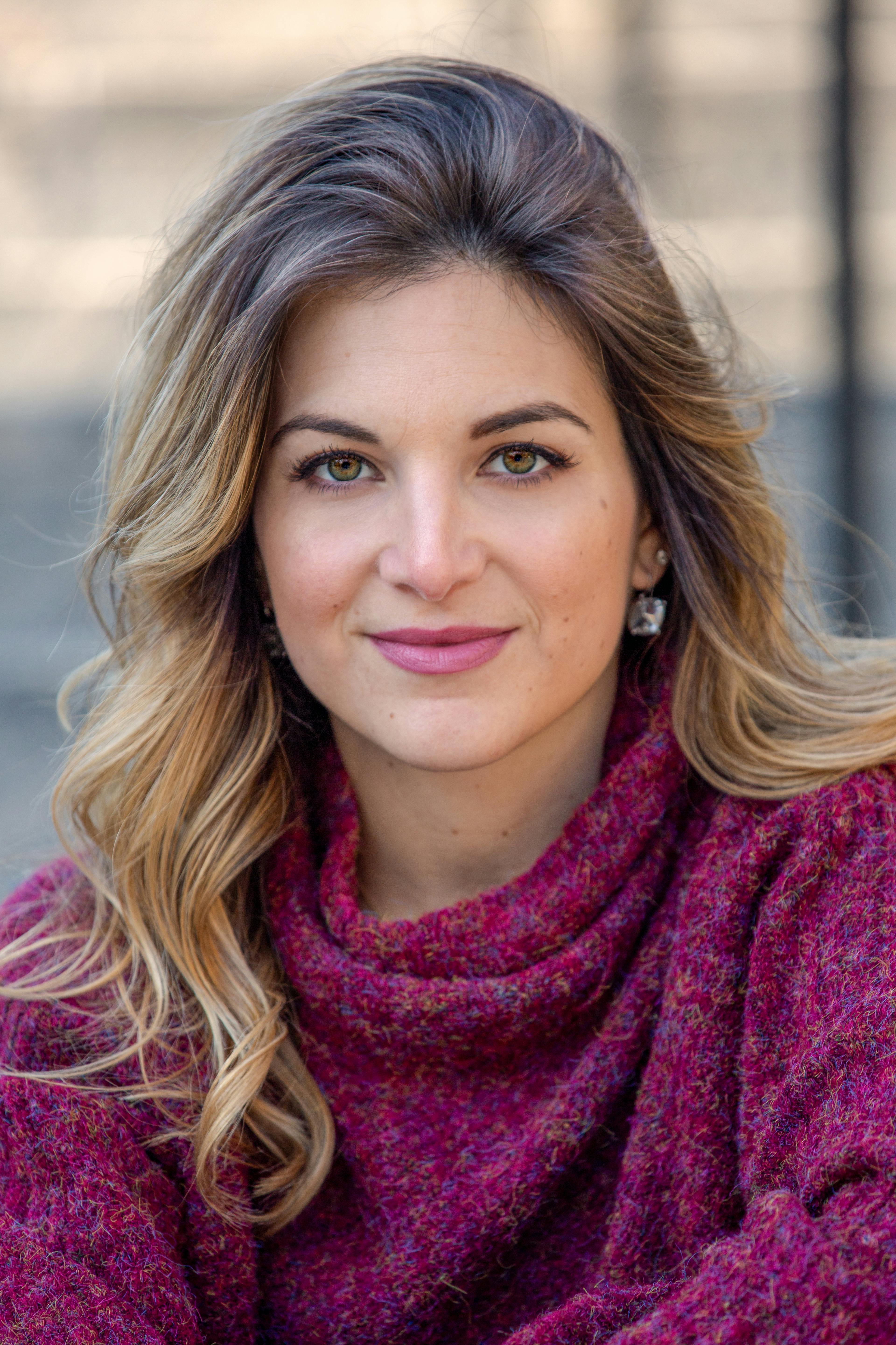 Close-up portrait of a young woman in a burgundy sweater outdoors.