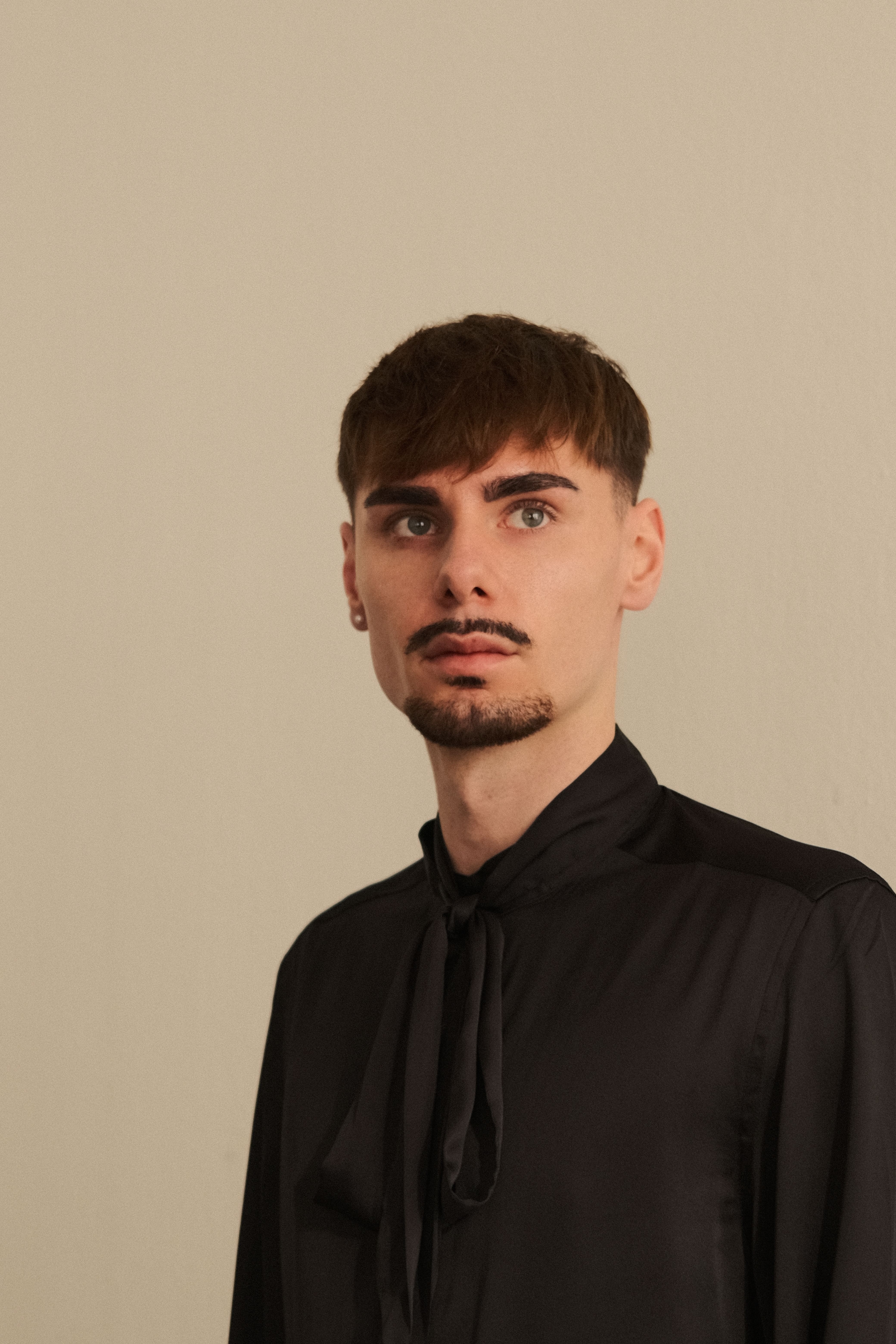 Stylish portrait of a young man in a black shirt, standing against a neutral background.